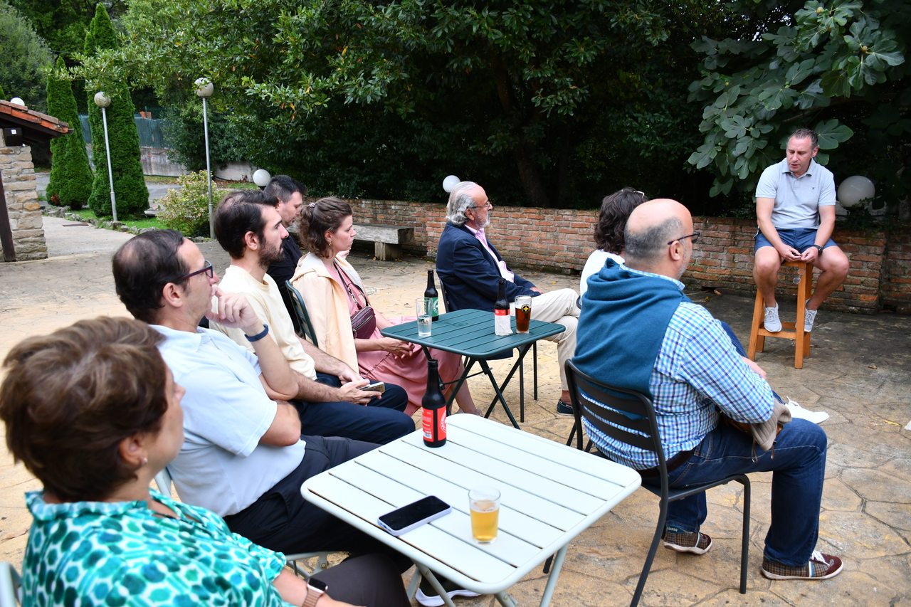 An outdoor audience listens to a speaker seated on a stool at Diáspora